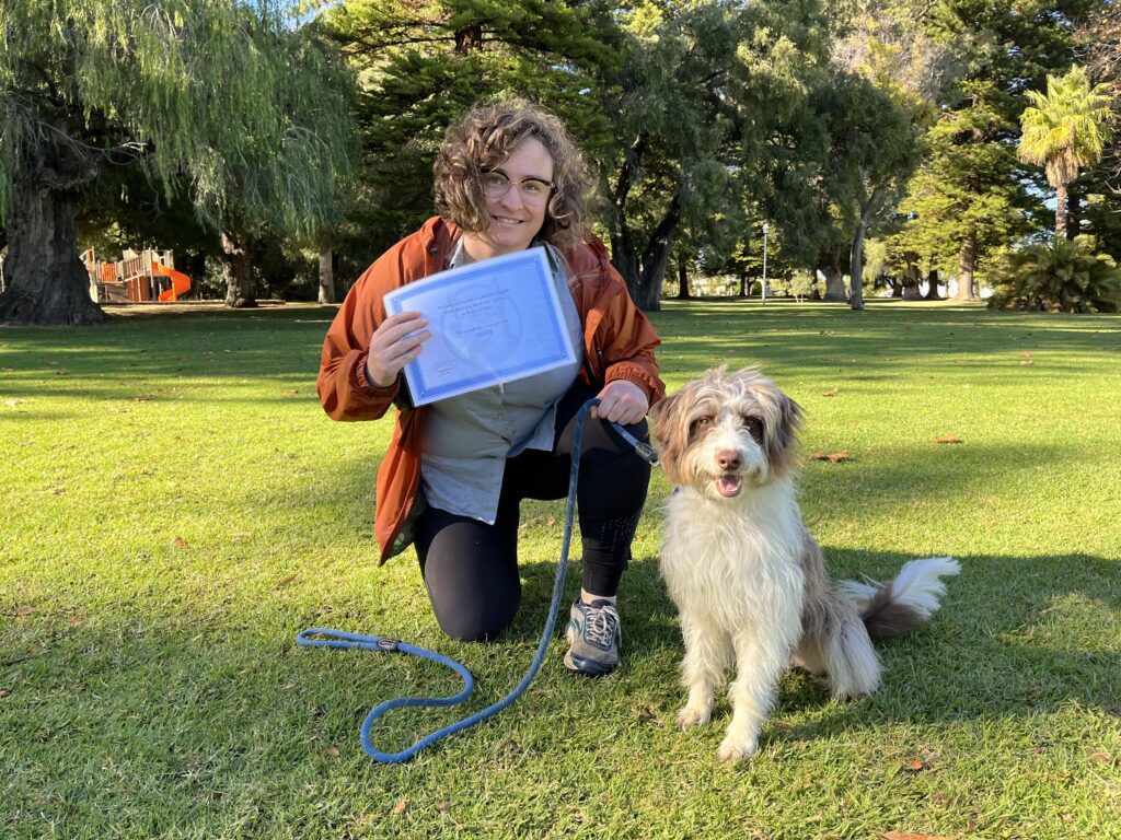 Dog training session outdoors with a woman and her Australian Shepherd in a lush park setting.
