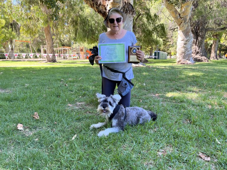 Happy woman with award and dog outdoors in park, showcasing successful training session.