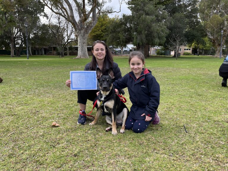 Two girls with a dog celebrating dog training success in a park.