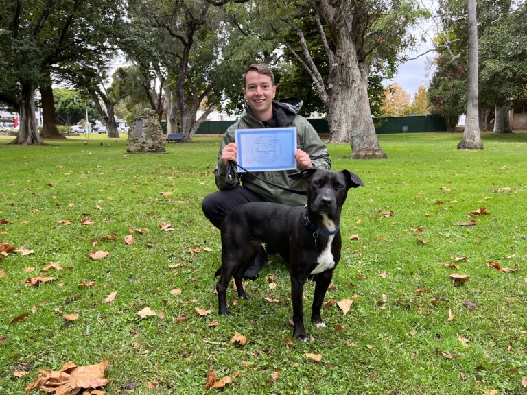 Man with black dog celebrating dog training certification outdoors.
