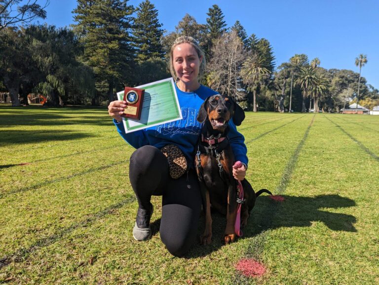 Dog training certification photo with a smiling woman and her trained dog outdoors.