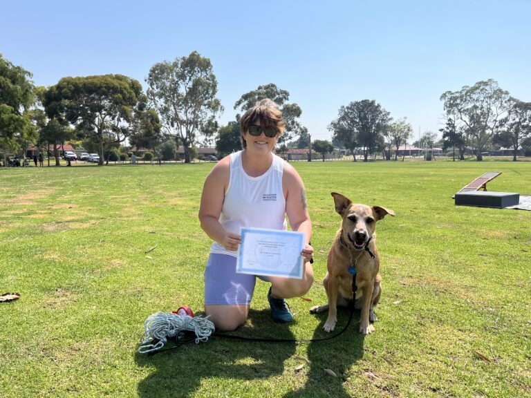 Woman with her trained dog holding a certificate in a park setting.