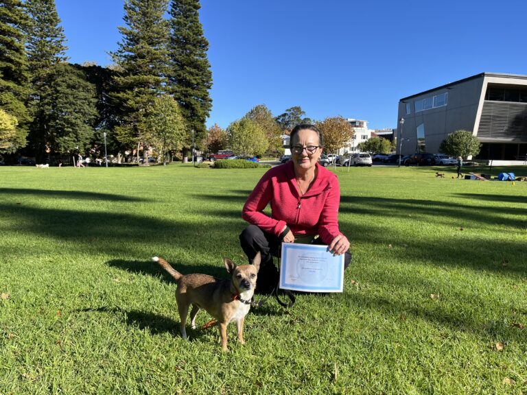 Woman with dog celebrating dog training success outdoors in park.