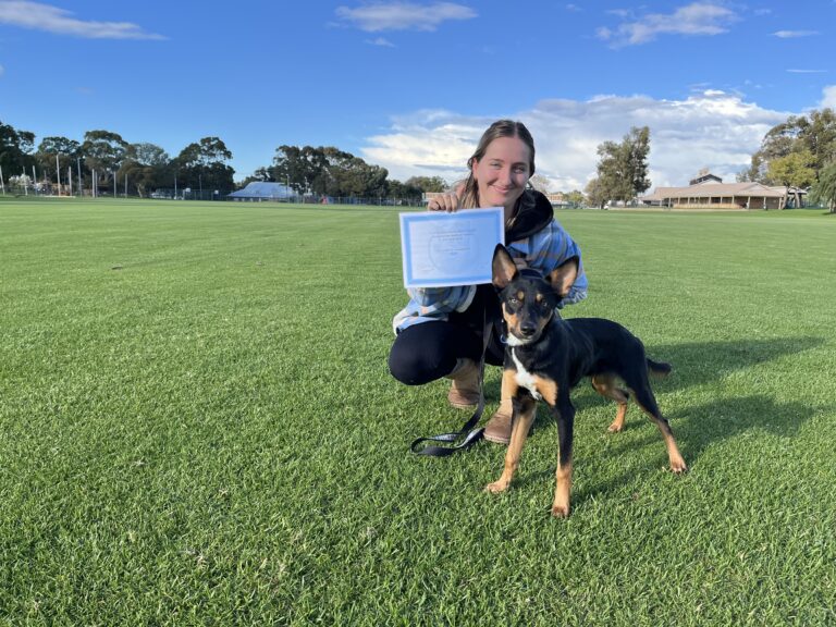 Woman with dog celebrating training success on a grassy field.