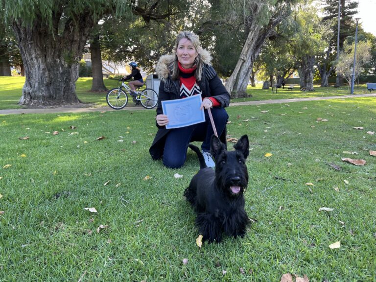 Woman with Scottish Terrier celebrating dog training success in park.