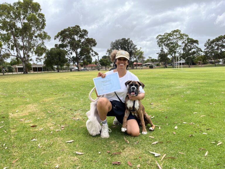 Woman celebrating dog training success outdoors with her dog and certificate.