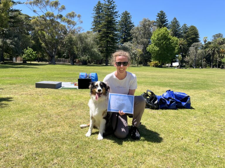 Woman with Australian Shepherd celebrating dog training success outdoors.